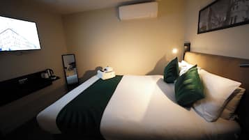 Quarto de hotel com uma cama, uma televisão fixada na parede, aparelho de ar condicionado e um quadro pendurado na parede.
