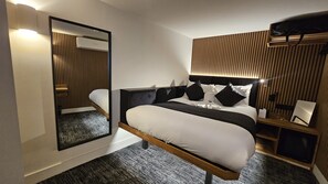 A modern hotel room with a large bed, a bedside table, a mirror, and a wall-mounted air conditioning unit. - Keystone House (London)