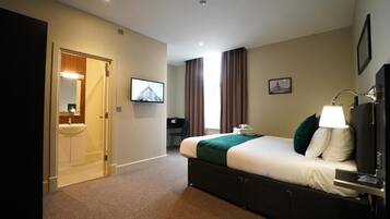 A hotel room with a bed, a desk, a TV, and a bathroom.