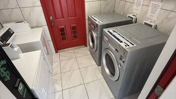 Een wasserette met een rode deur, twee wasmachines en een droger.