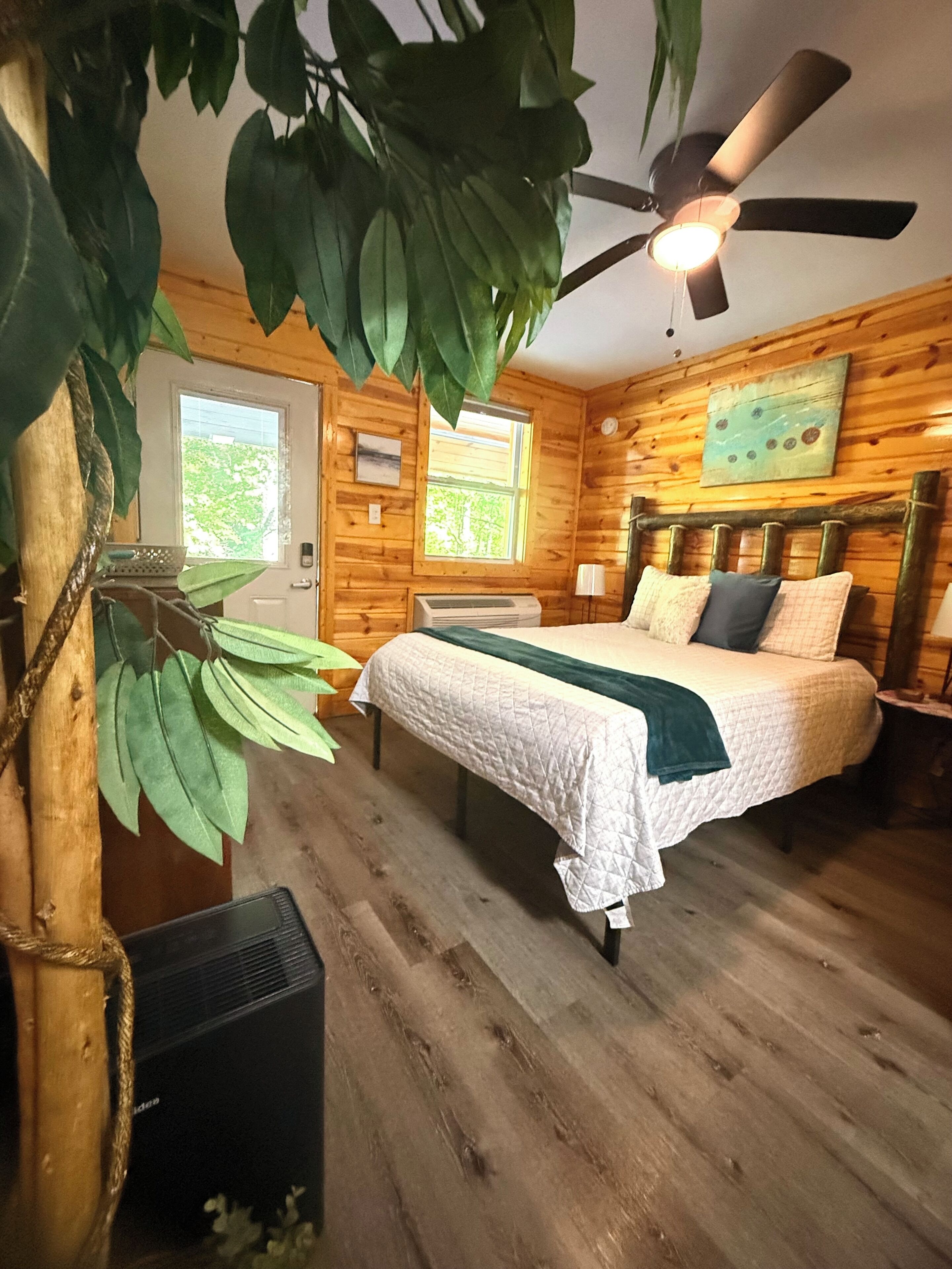 Habitación de cabaña de madera con cama, ventilador de techo, ventana y puerta.