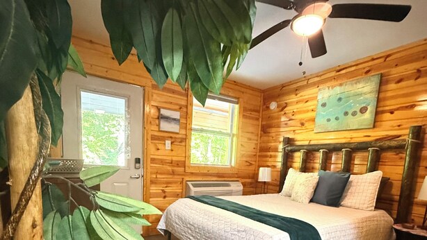 A wooden cabin room with a bed, a ceiling fan, a window, and a door. - Rustic Studio 4, Pets Welcome (Tennessee)