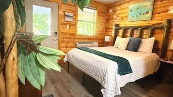 Habitación de cabaña de madera con cama, ventilador de techo, ventana y puerta.