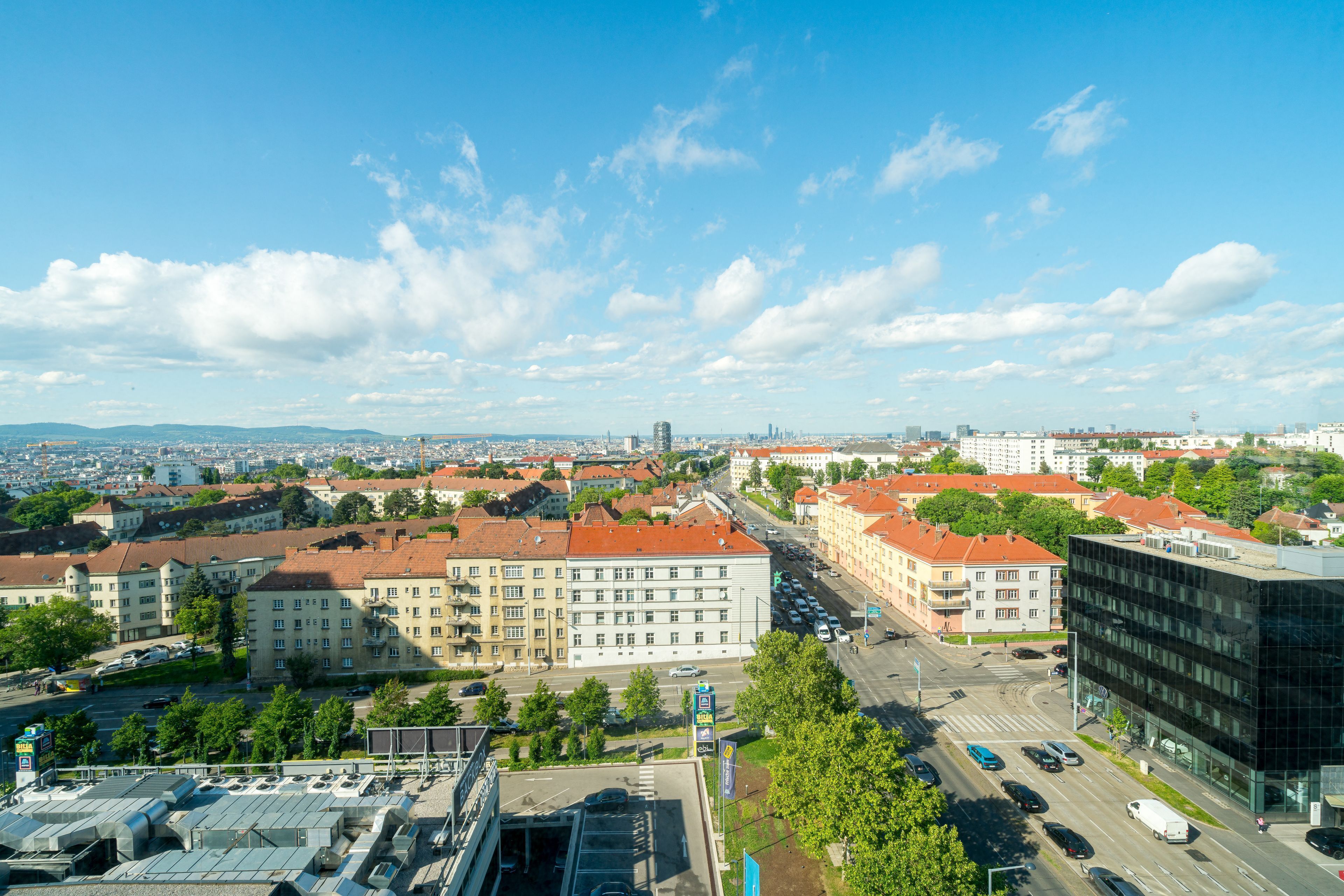 Un paisaje urbano que combina edificios modernos y tradicionales, cielo despejado y una calle concurrida llena de coches y peatones.