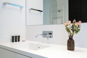 A bathroom with a white sink, a mirror, and a vase with flowers. - Vienna Residence, Philips Haus - Europlaza (Vienna)
