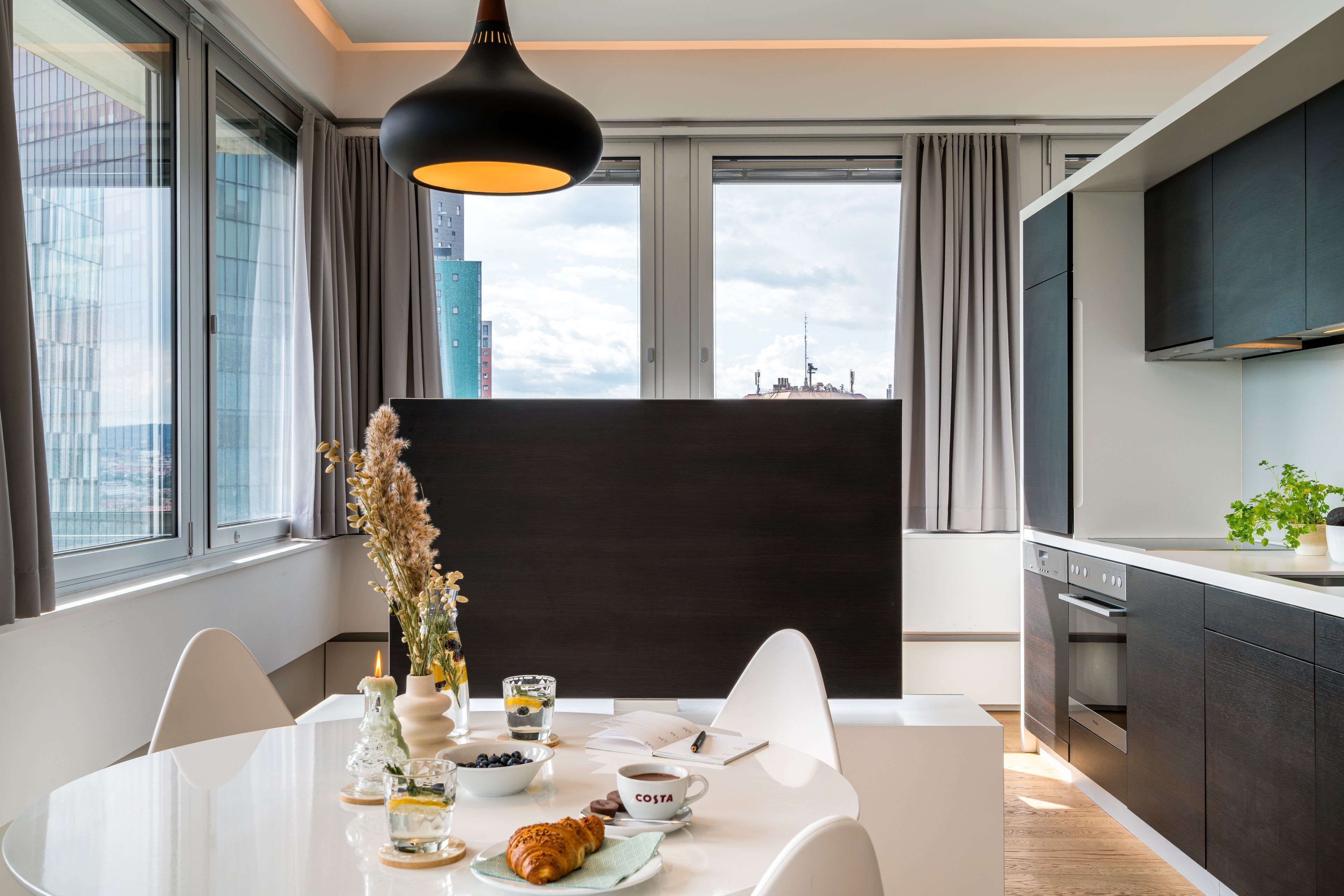 A modern dining area with a white table, chairs, and a city view through large windows.