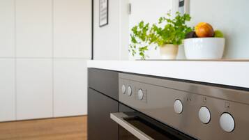 A kitchen with a stainless steel oven, a white countertop, and a bowl of fruit and a plant on the counter.