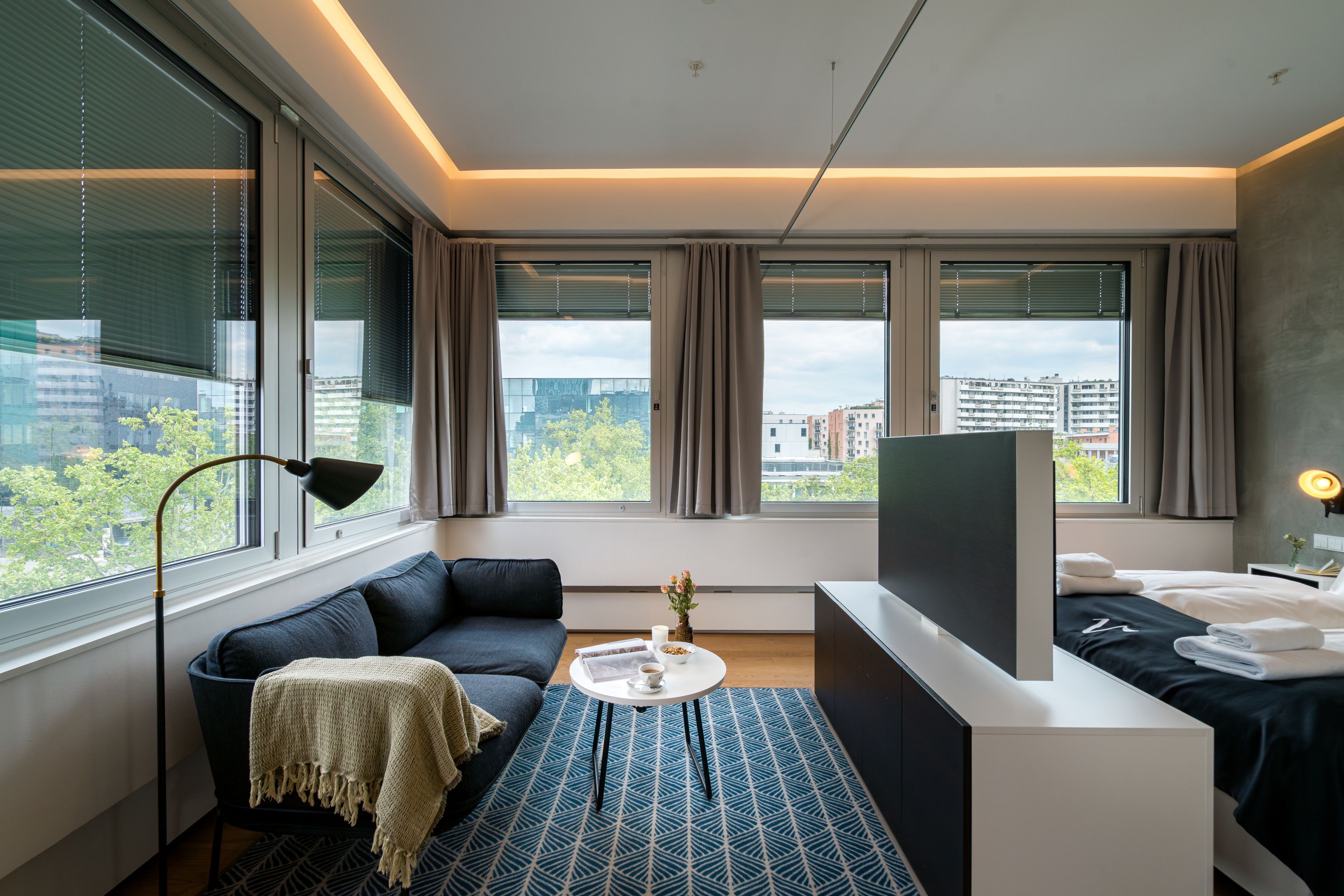 A modern hotel room with a sofa, a small table, a TV, and a bed.