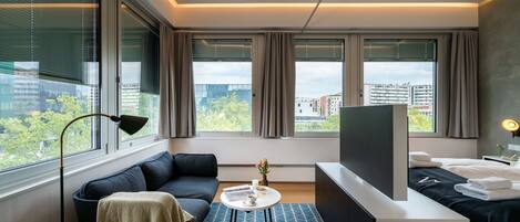 A modern hotel room with a sofa, a small table, a TV, and a bed.