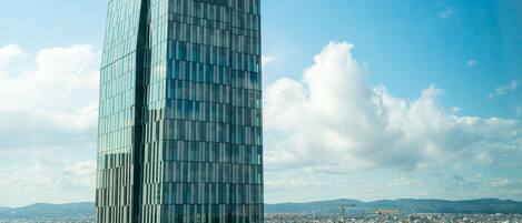 A modern glass skyscraper with a grid-like facade, set against a backdrop of a cityscape and distant mountains.
