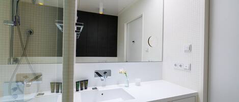 A modern bathroom with a white sink, a large mirror, and a glass-enclosed shower area.