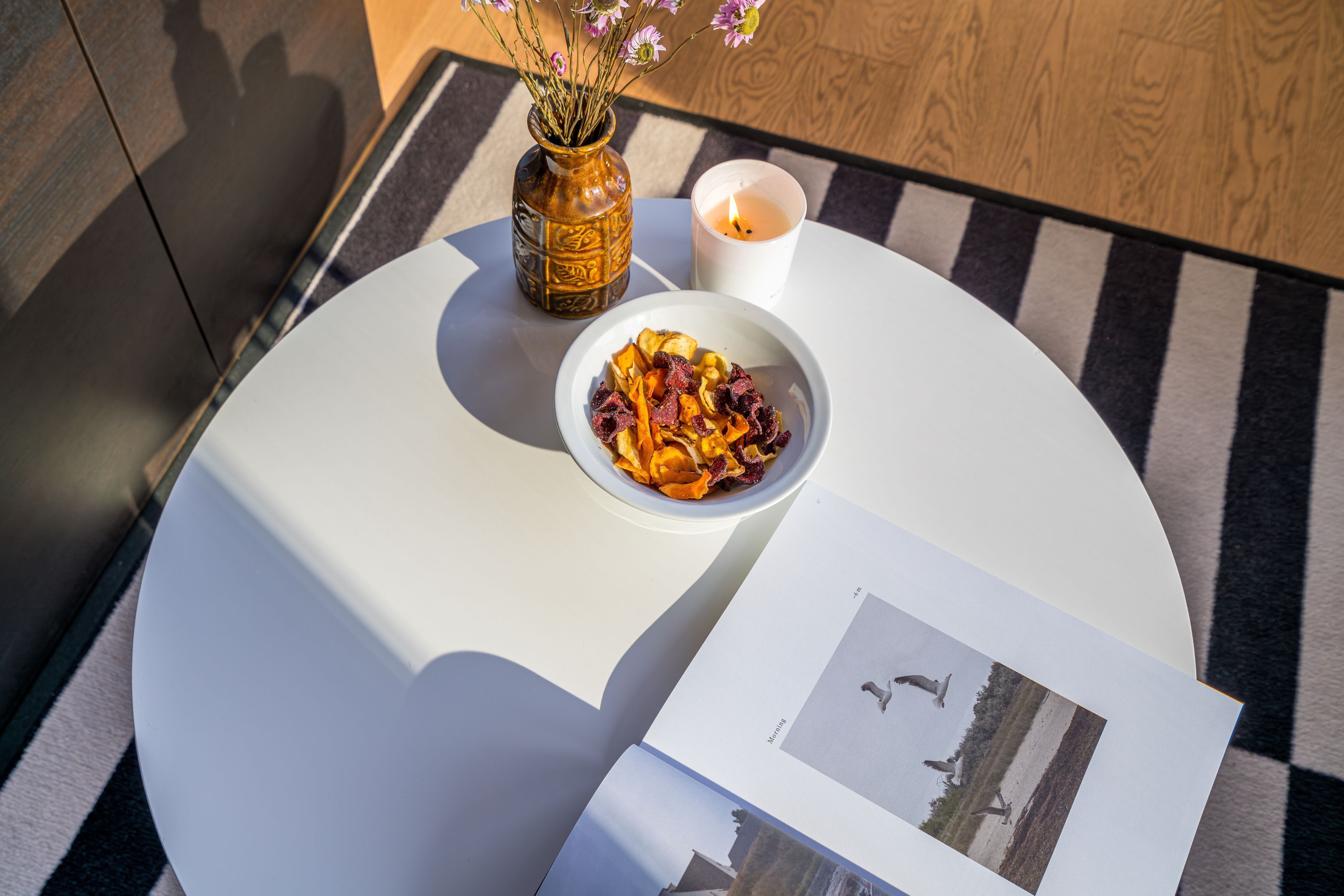Ein runder Tisch mit einer weißen Schüssel voller Trockenfrüchte, einer Kerze und einer Blumenvase.