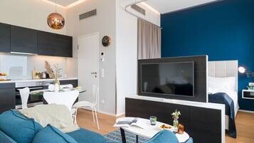Een moderne woonkamer met een bank, een flatscreen televisie, een eettafel en een keuken met kasten en een fornuis.