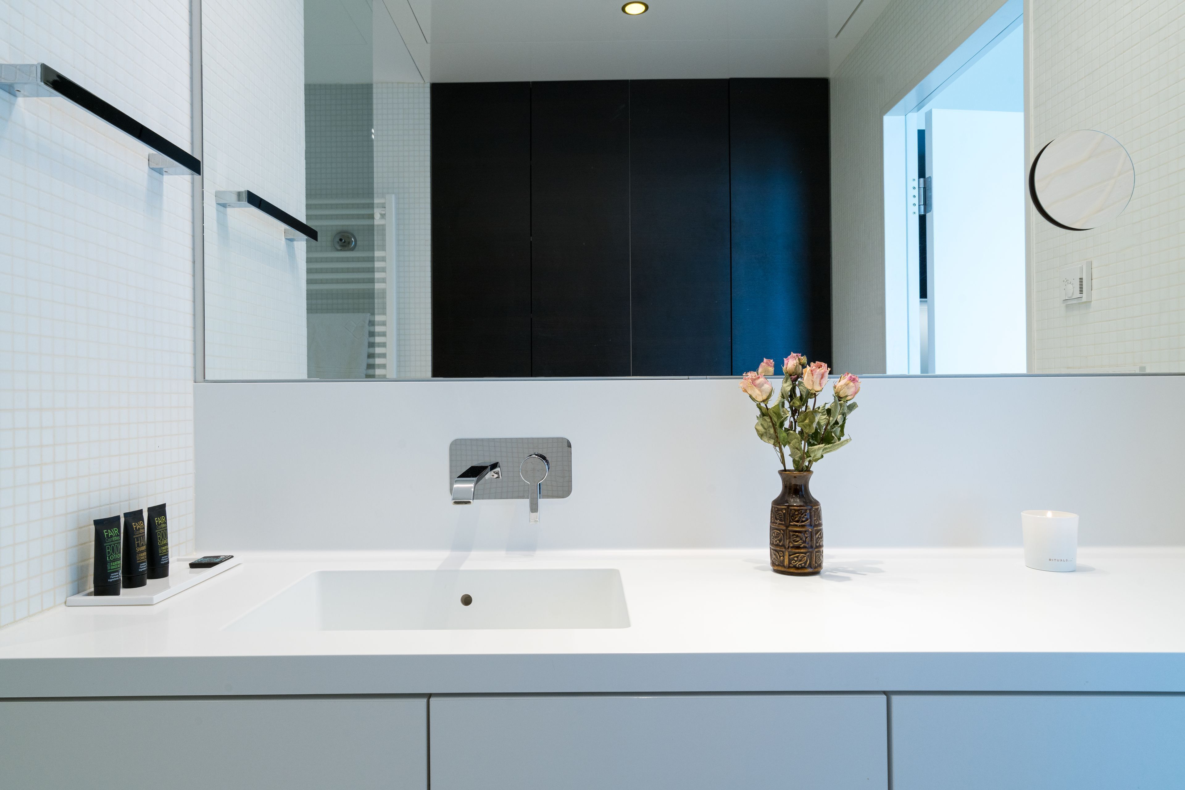 A modern bathroom with a white sink, a mirror, and a vase of flowers.