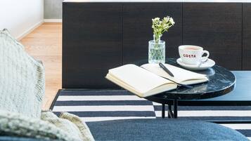 A modern living room with a dark wooden cabinet, a round black table with a book and a cup labeled "COSTA", and a striped rug.
