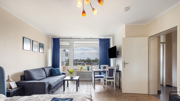 Moderni hotellihuone, jossa on sänky, sohva, ruokailutila ja parveke, jolta on näkymä.