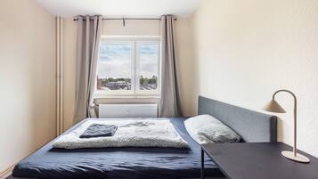 Un dormitorio con cama, mesita de noche, lámpara y ventana con cortinas.