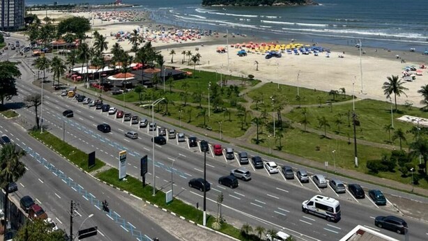 Un paysage urbain côtier avec une plage, une autoroute et les contours d’une ville lointaine à l’horizon.
