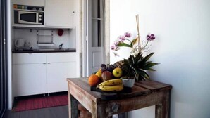 A kitchen with white cabinets, a microwave, and a small table with fruit and a potted plant. - Oporto Private Room/TERRACE (Porto)