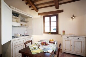 A dining area with a table set for two, a window with a view, and a kitchen area with cabinets and a shelf. - Montedoro - Cerchiare (Montefiascone)