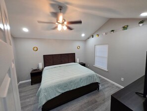 A bedroom with a bed, a nightstand, a ceiling fan, a window with blinds, and a small plant on the wall. - Lovely 2-bedroom triplex unit with AC in charming Van Buren. (Van Buren)