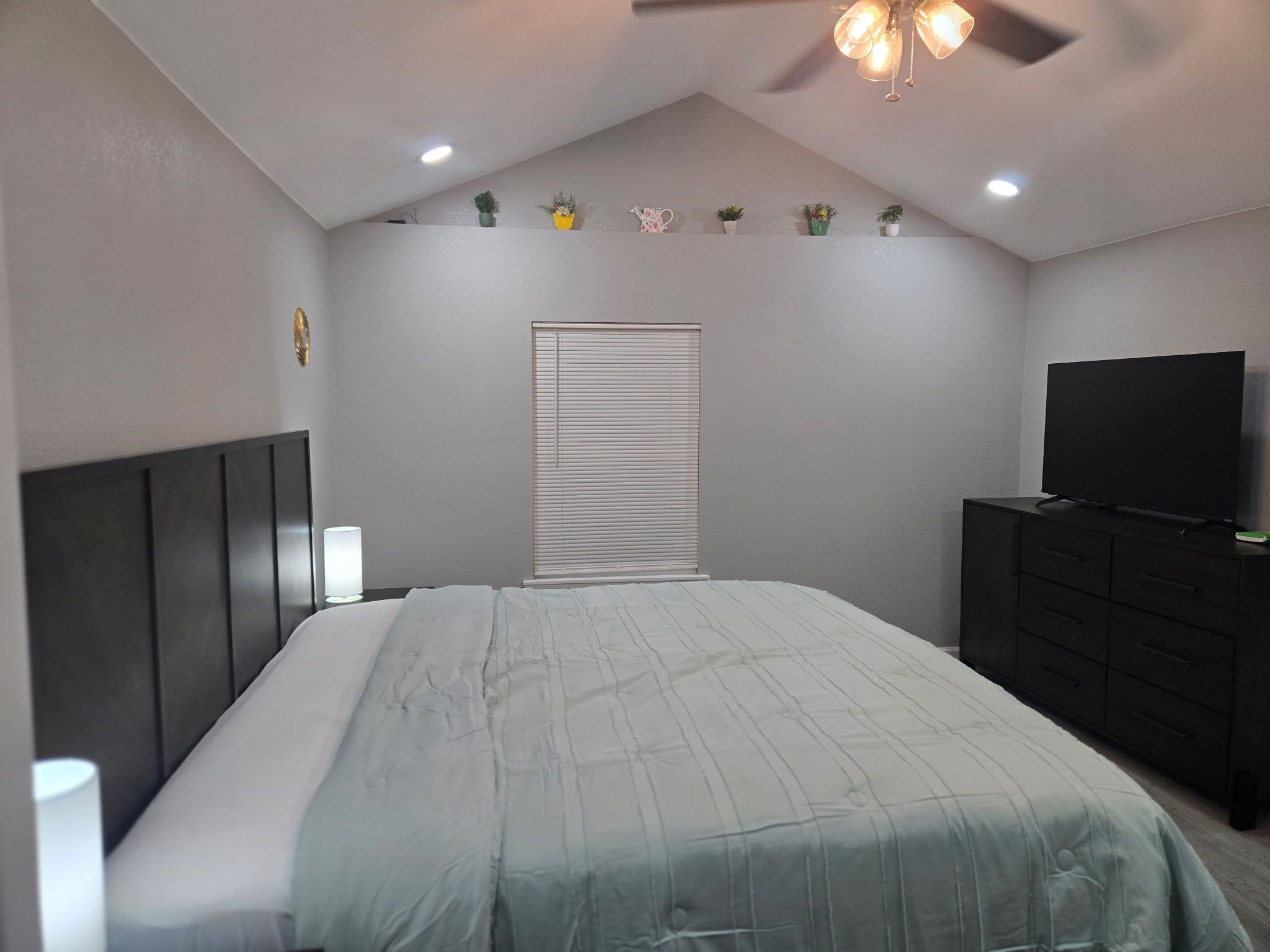 A bedroom with a bed, a dresser, a television, and a ceiling fan.