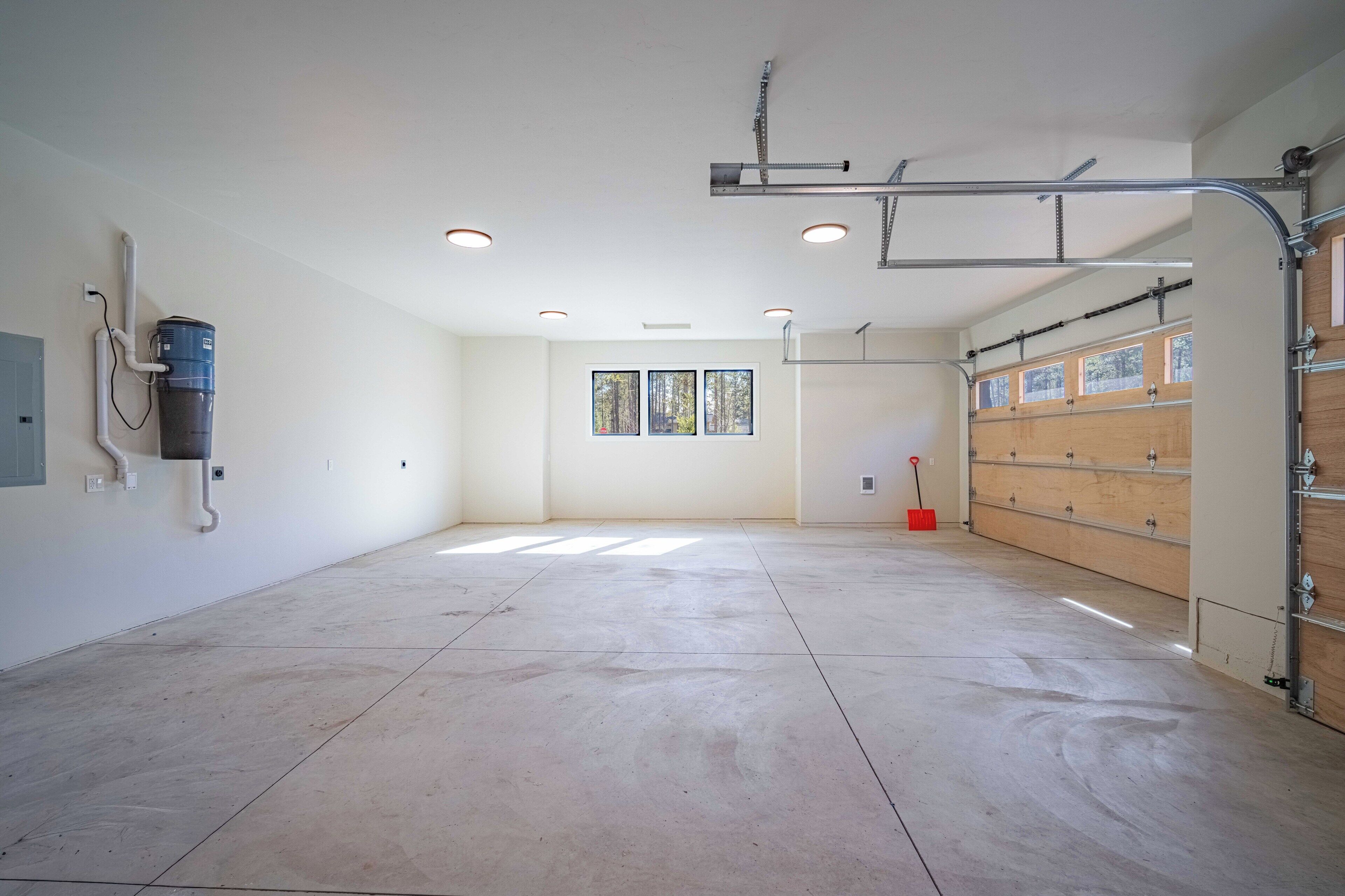 A spacious, well-lit room with a large window, a ceiling-mounted air conditioning unit, and a wooden door.
