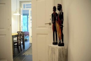 A hallway with a dining area visible through an open door. There are two statues on a pedestal against the wall. - Oporto Center Private Room 1 (Porto)