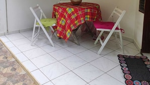 A small, enclosed patio area with a table and two chairs, a window, and a tiled floor. - Les Ziottines (Deshaies)