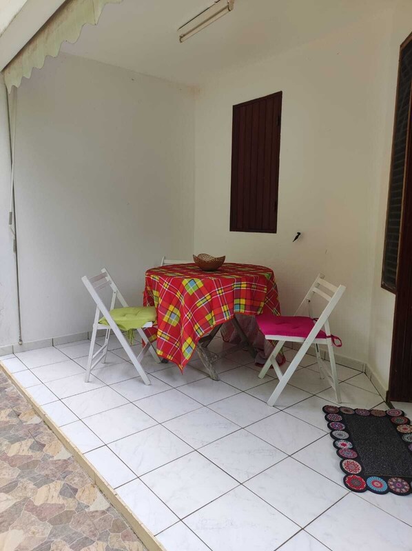 A small, enclosed patio area with a table and two chairs, a window, and a tiled floor. - Les Ziottines (Deshaies)