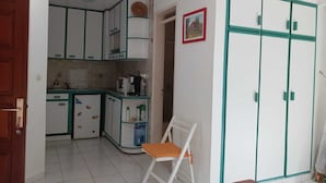 A compact kitchen with white cabinets and a small dining area with a white chair. - Les Ziottines (Deshaies)
