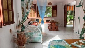 A room with a bed, a small table, a chair, and a window with curtains. - Les Ziottines (Deshaies)
