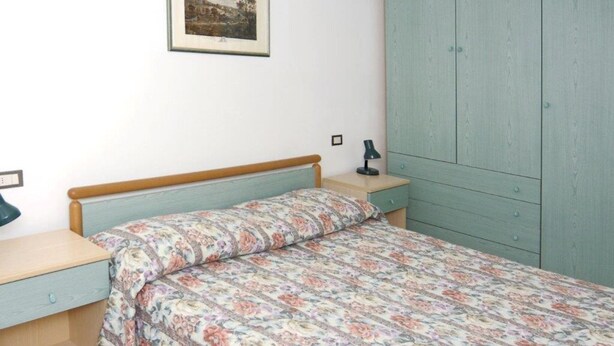 A bedroom with a bed, a nightstand, a lamp, a wardrobe, and a framed picture on the wall. - Comfortable Flat With Shared Pool (San Michele al Tagliamento)