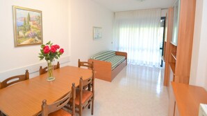 A room with a wooden dining table, chairs, a sofa, and a bed. - Comfortable Flat With Shared Pool (San Michele al Tagliamento)