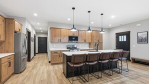 A modern kitchen with wooden cabinets, stainless steel appliances, and a central island with bar stools. - Newly Built, Spacious Duplex, Huge Garage, Hot Tub, Clubhouse Access! (Lead)