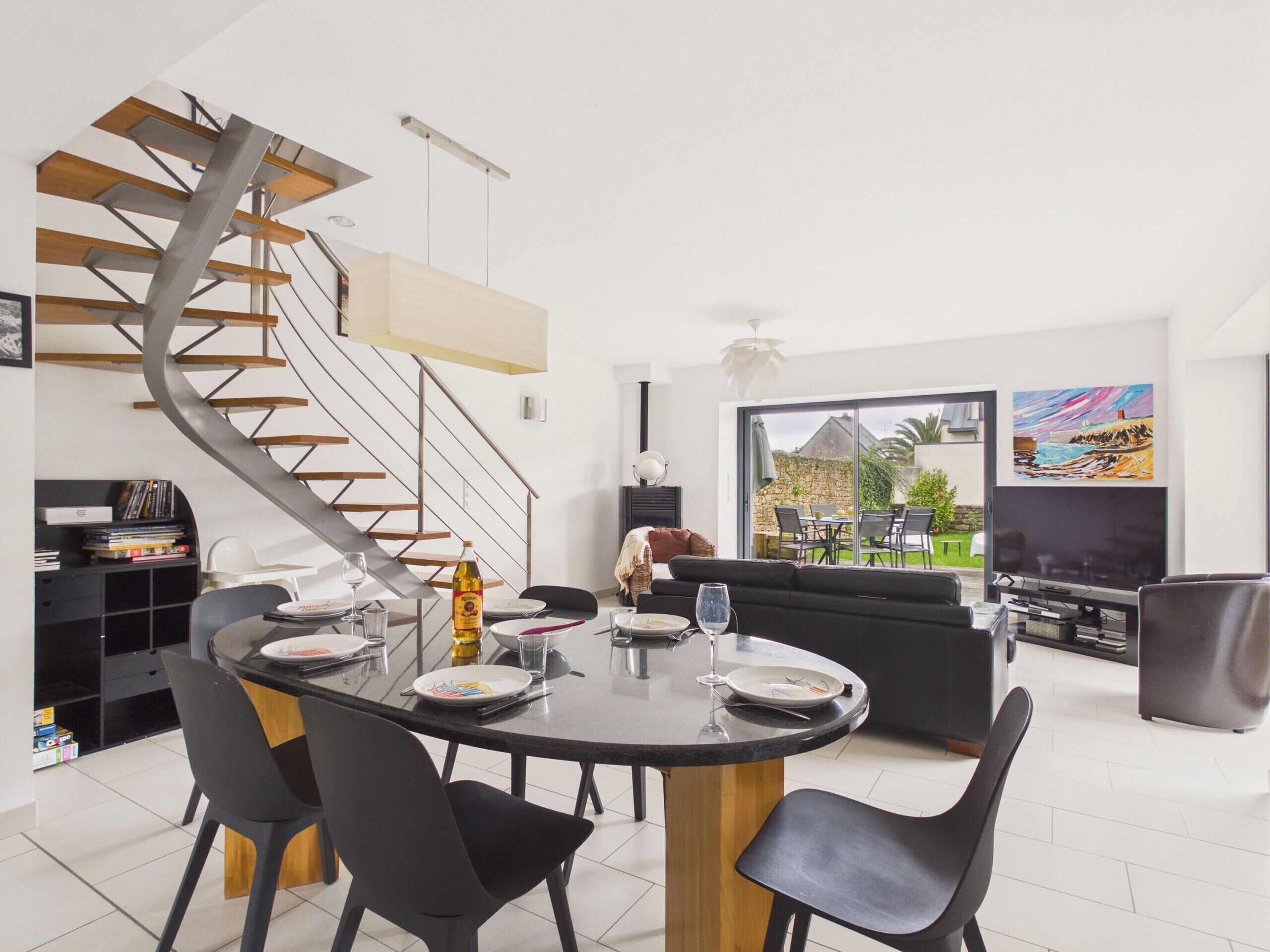 Una cocina moderna con una escalera espiral, un comedor con una mesa redonda y un amplio ventanal con vistas al exterior.