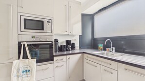 Eine moderne Küche mit weißen Schränken, einer Mikrowelle, einem Backofen, einer Kaffeemaschine und einem Spülbecken.