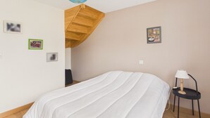 Ein Schlafzimmer mit einem Bett, einer Holztreppe, einem kleinen Tisch mit einer Lampe und einer Wand mit gerahmten Bildern.