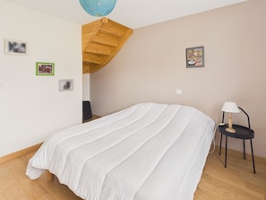 A bedroom with a bed, a wooden staircase, a small table with a lamp, and a wall with framed pictures. - House 6 guests, garden, shops by foot (Fouesnant)