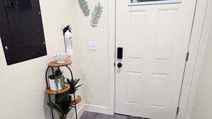 A hallway with a white door, a black wall-mounted panel, a potted plant shelf, a fire extinguisher, and a small window with a view. - Sage & Cedar
Cozy home ready for your stay (Webb City)
