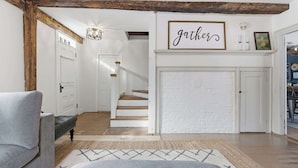 A spacious living area with a staircase, a grey sofa, and a 'gather' sign above a fireplace. - Spacious Farmhouse Near the Beach Circa 1860 (Biddeford)