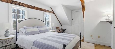 A bedroom with a bed, a nightstand, a lamp, and a window.