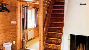 L’intérieur d’un chalet en bois, avec une cheminée, un escalier et une fenêtre avec des rideaux.