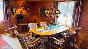 L’intérieur chaleureux d’un chalet avec une table à manger en bois entourée de chaises à rayures, un crâne de cerf accroché au mur et un tableau.