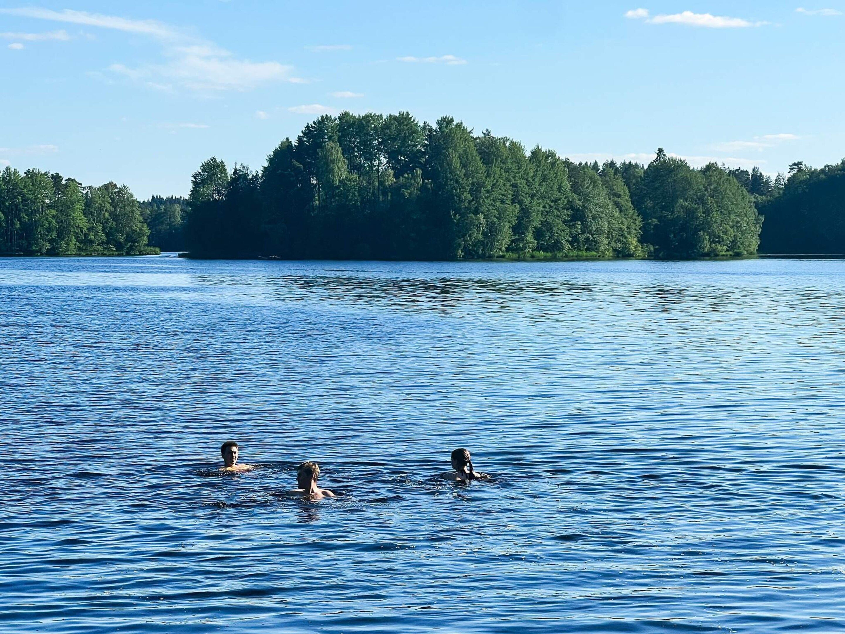 A lake with three people swimming, surrounded by dense forest.