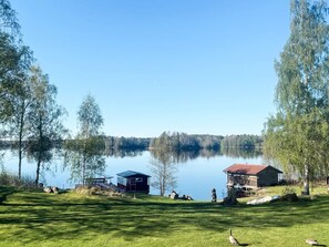 A lakeside property with a wooden cabin, a small shed, and a grassy area. - 7 Person Holiday Home in Lekeryd (Lekeryd)