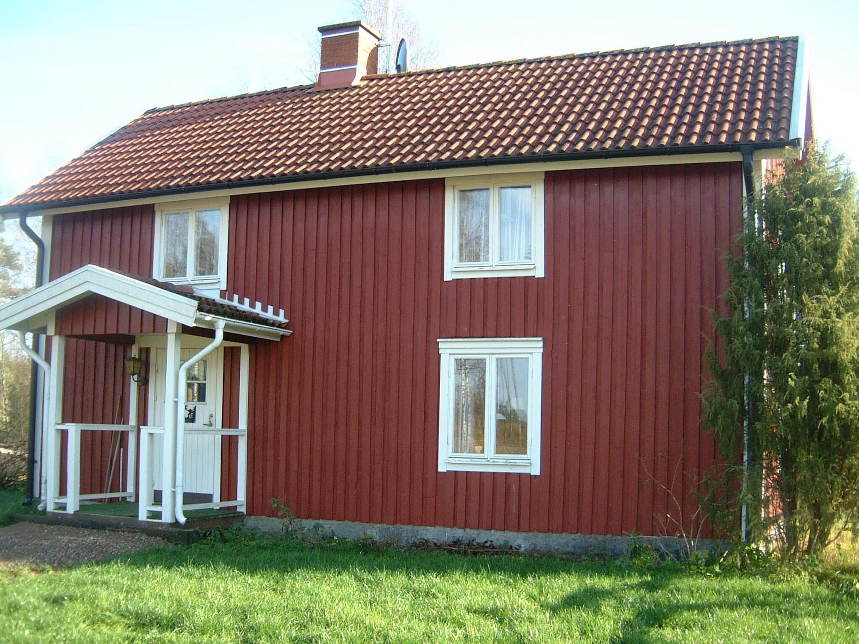 A red two-story house with a tiled roof, white windows, and a small porch with a white railing.