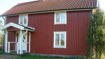A red two-story house with a tiled roof, white windows, and a small porch with a white railing.