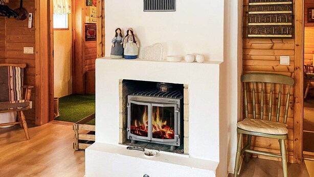 A cozy room with a fireplace, wooden walls, a chair, and a shelf with decorative items. - 7 Person Holiday Home in Lekeryd (Lekeryd)