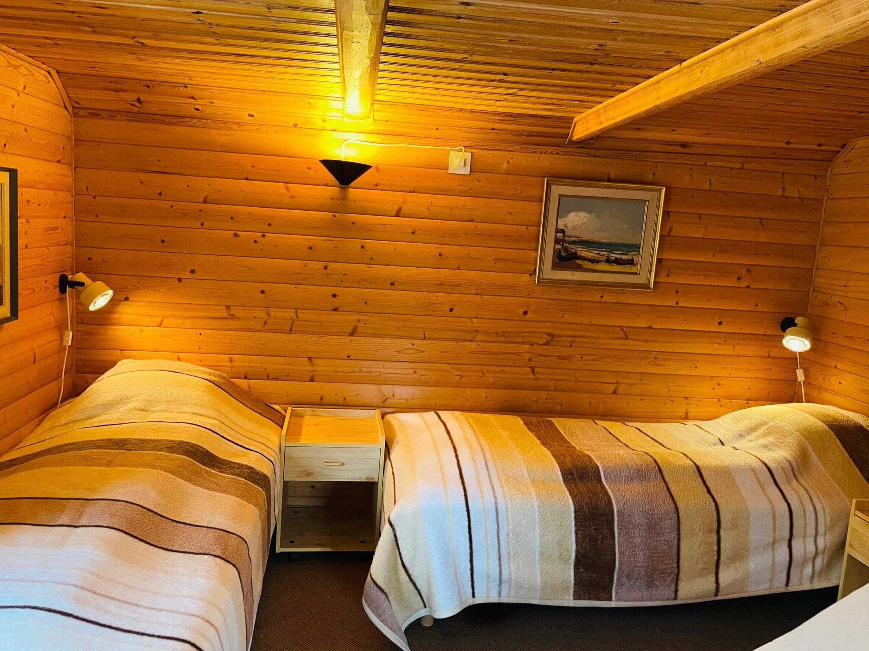 A cabin room with two beds, a nightstand, a lamp, and a framed picture on the wall.